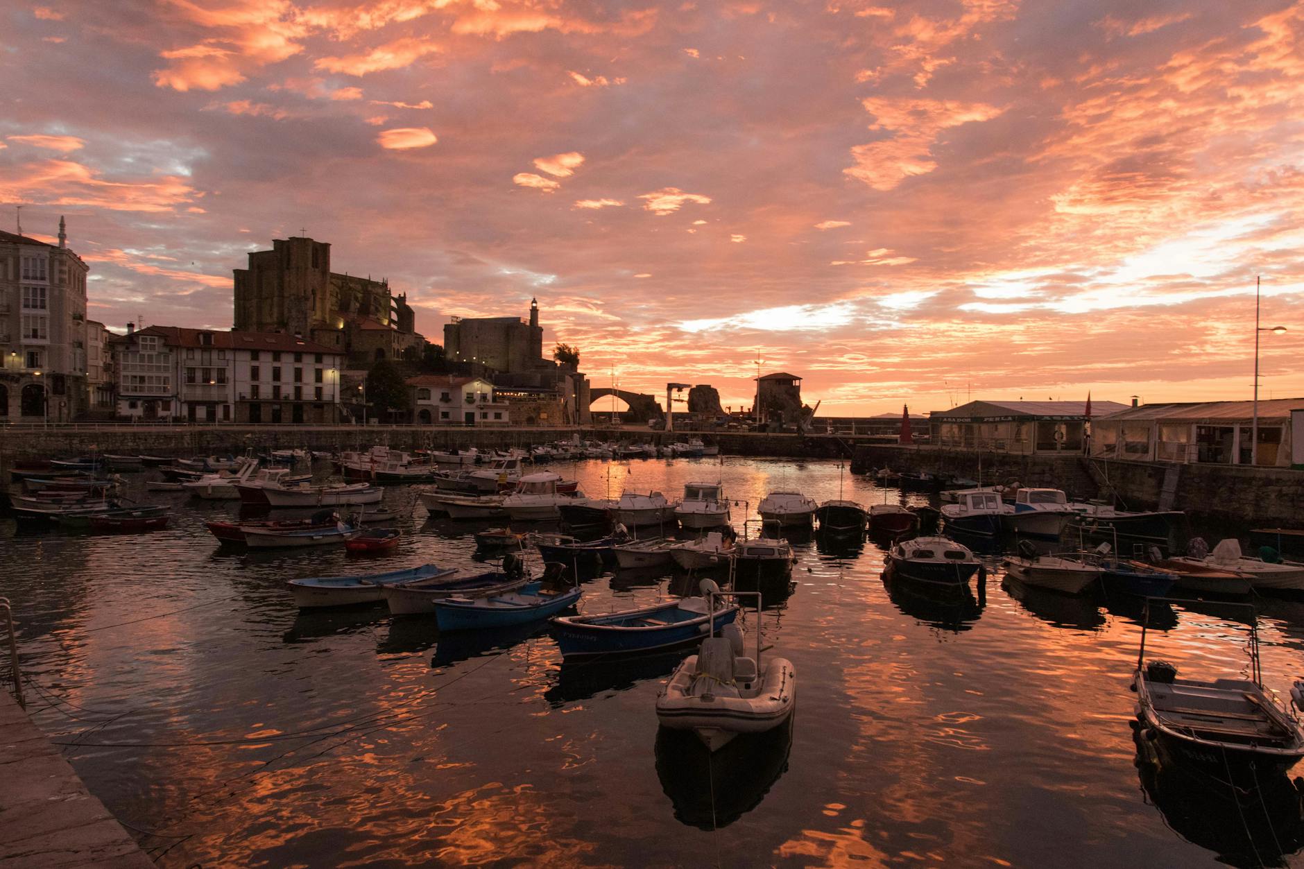 A vibrant sunset over Castro Urdiales harbor with boats and buildings, capturing a serene waterfront scene.